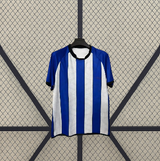 Vista frontal en percha de la camiseta RCD Espanyol 26-27 local con franjas azules y blancas, cuello oscuro y puños en contraste