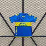Vista frontal extendida de la camiseta Las Palmas 26-27 visitante, con banda amarilla en el pecho y detalles amarillos en hombros y puños