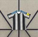 Vista frontal extendida de la camiseta Newcastle 26-27 local con franjas blancas y negras de distintos grosores y ribetes azul celeste