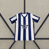 Vista frontal extendida de la camiseta Real Sociedad 26-27 local con franjas blancas y azul marino, puños oscuros y paneles laterales