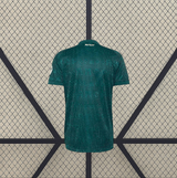 Vista trasera de la camiseta R.M. 26-27 visitante en verde oscuro, con textura geométrica tonal y detalle dorado bajo el cuello