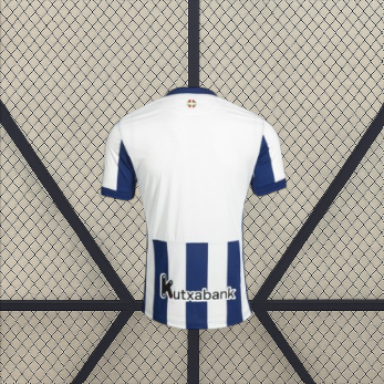 Vista trasera de la camiseta Real Sociedad 26-27 local con zona superior blanca, mangas azul marino y franjas en la parte inferior
