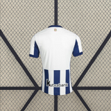Vista trasera de la camiseta Real Sociedad 26-27 local con zona superior blanca, mangas azul marino y franjas en la parte inferior