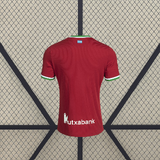 Vista trasera de la camiseta Real Sociedad 26-27 tercera equipación en rojo con manga corta y detalles verdes y blancos en cuello y puños
