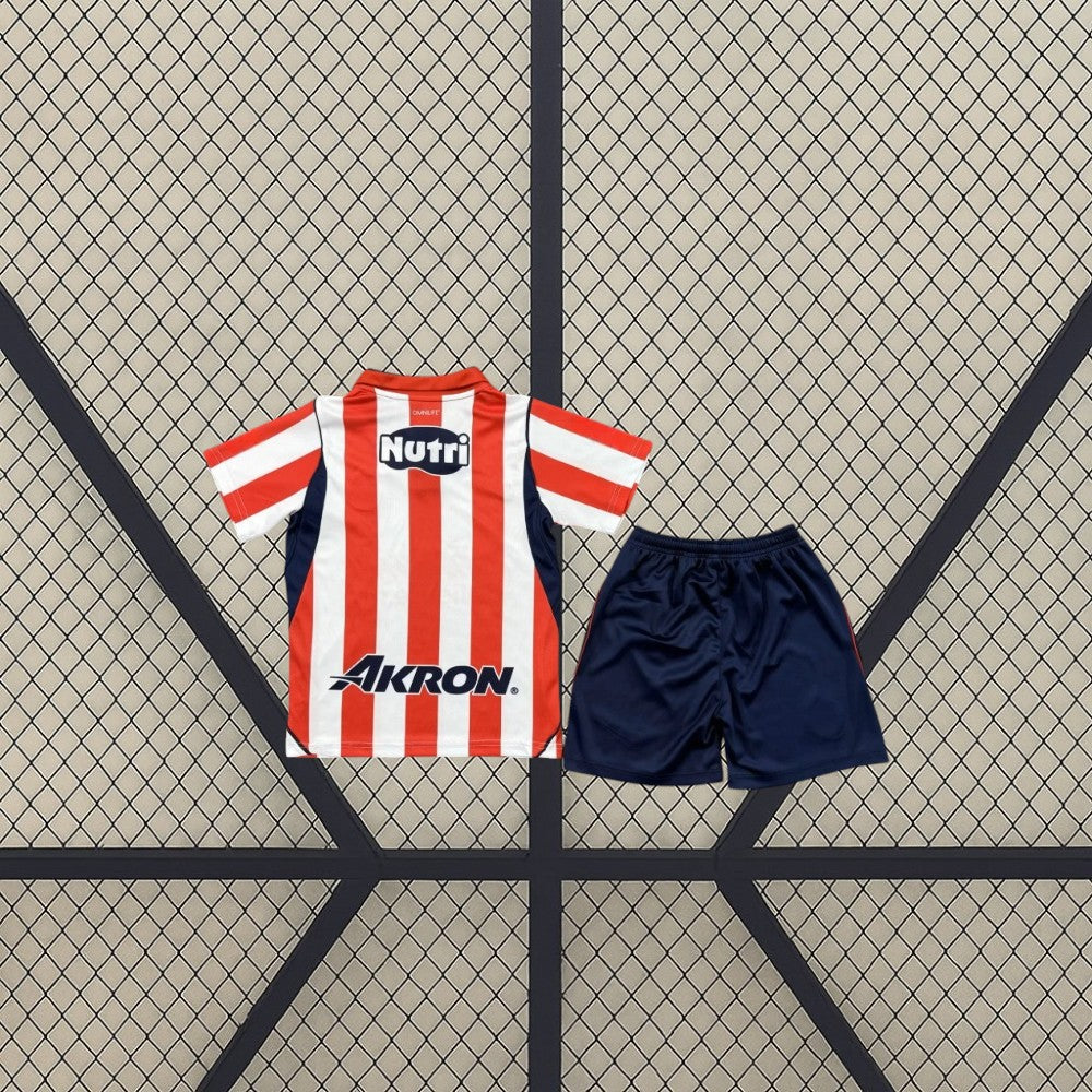 Vista trasera de la equipación Chivas Guadalajara 26-27 Local de niño con camiseta de franjas rojas y blancas y pantalón azul marino
