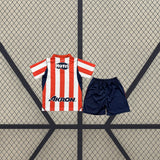 Vista trasera de la equipación Chivas Guadalajara 26-27 Local de niño con camiseta de franjas rojas y blancas y pantalón azul marino