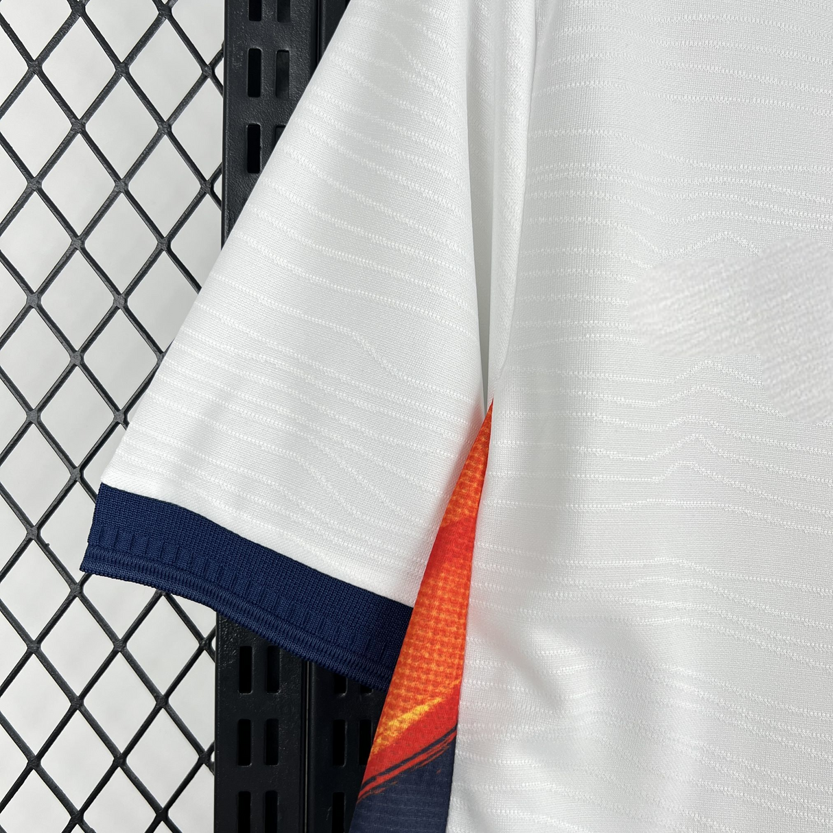 Detalle de manga blanca con puño azul marino y panel lateral naranja de la camiseta Ecuador 26-27